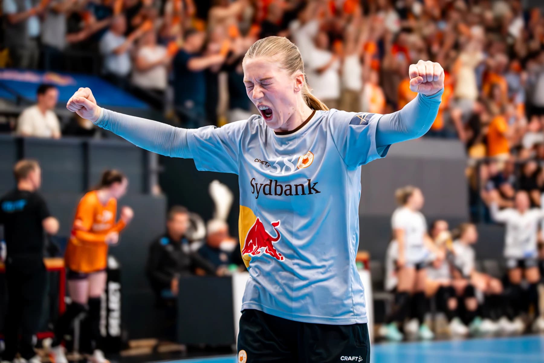 Håndboldspiller jubler i klubtrøje med logo på brystet foran publikum i arena